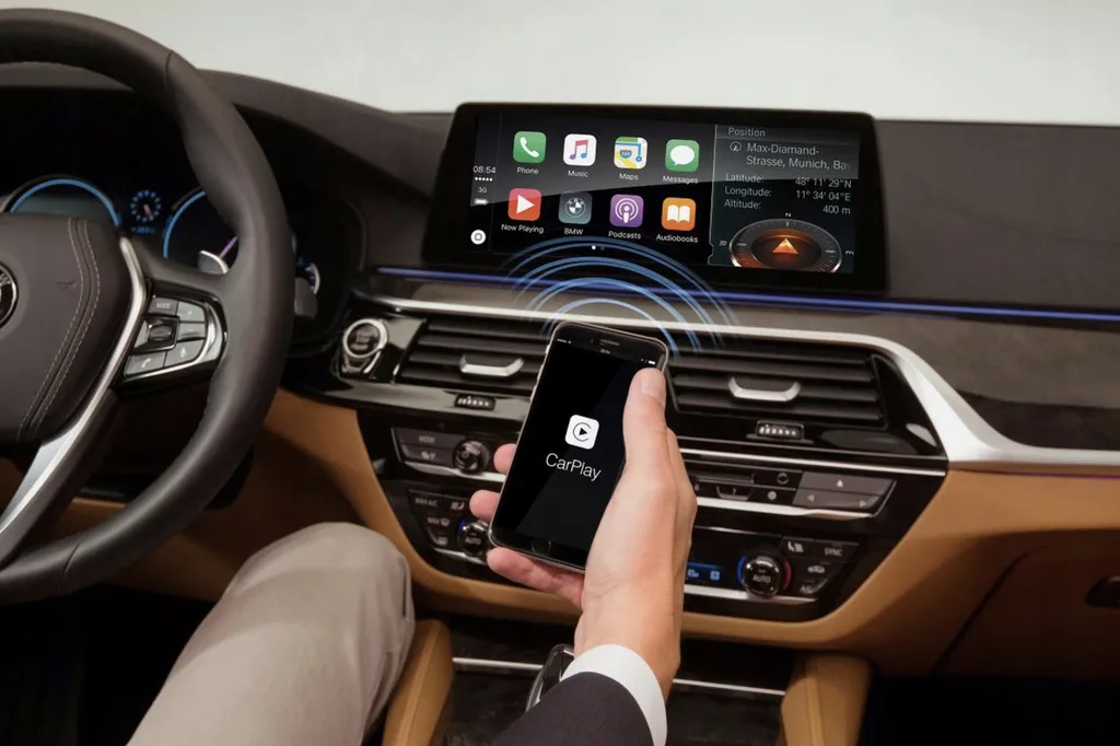 Dłoń trzyma iPhone’a z logo CarPlay przed ekranem BMW, na którym wyświetlają się ikony aplikacji CarPlay